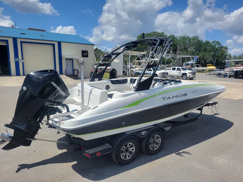 Slide: The Image of 2021 Tahoe 2150 boat on trailer, parked outdoors under a partly cloudy sky. - 4