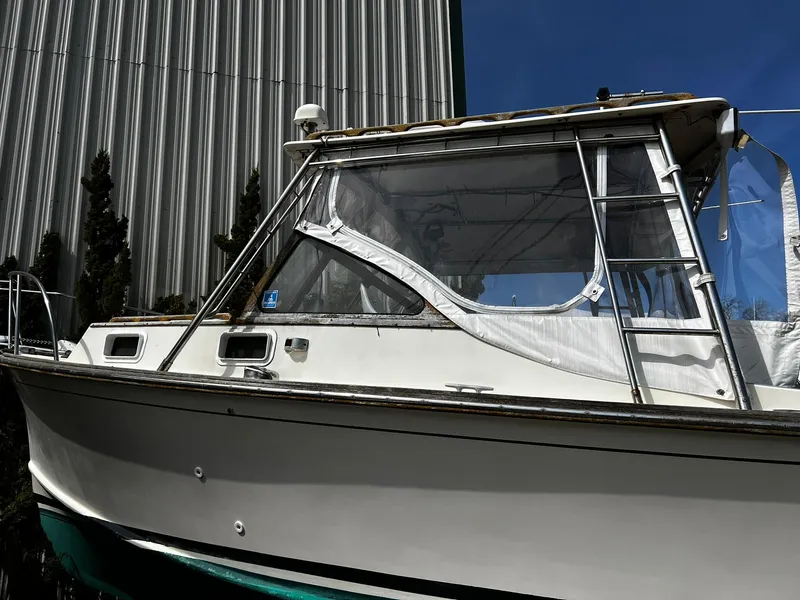 Slide: The Image of 1983 Fortier 26 boat with enclosed cabin, docked near a metal building. - 5