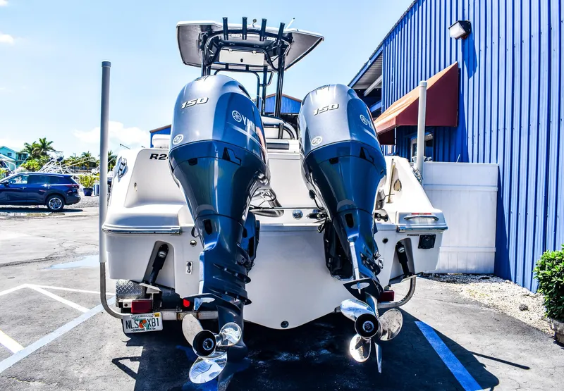 Slide: The Image of 2019 Robalo R242 Center Console boat with twin outboard engines, parked near a blue building. - 2