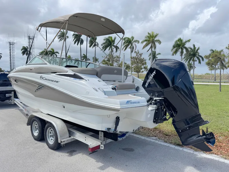 Slide: The Image of 2022 Crownline Eclipse E235 XS boat on trailer, parked near palm trees under cloudy sky. - 2