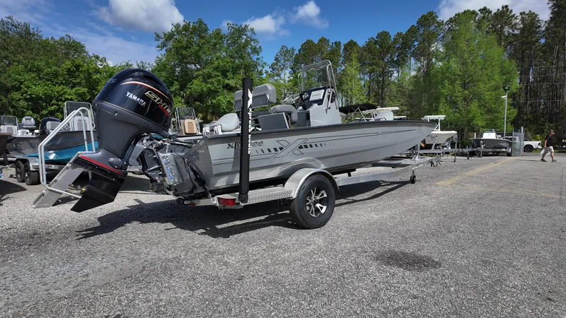 Slide: The Image of 2025 Xpress H20B boat on trailer, parked outdoors with trees in background. - 16