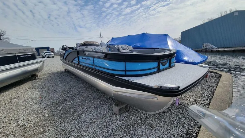 Slide: The Image of 2025 Bennington R Bowrider Swingback 24 RTSB pontoon boat on gravel near water. - 33