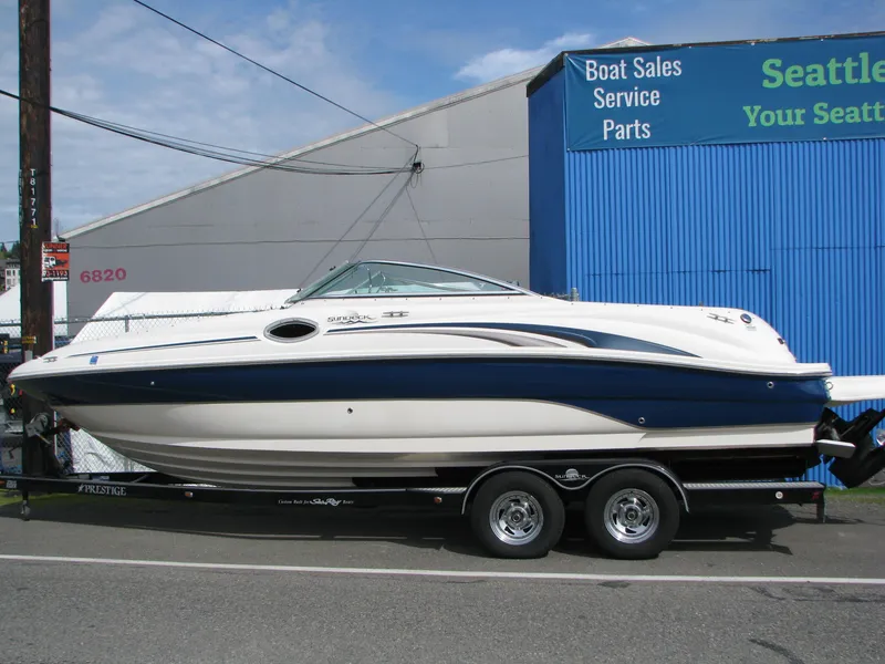 Slide: The Image of 2003 Sea Ray 240 Sundeck boat on trailer, parked outside a blue building. - 0
