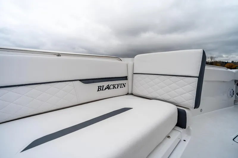 Slide: The Image of 2023 Blackfin 252 CC boat with white quilted seating and logo, under cloudy sky. - 17