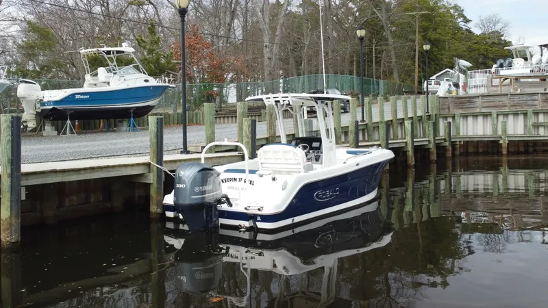 Slide: The Image of 2020 Robalo R242 Explorer boat docked in a marina, surrounded by calm water and trees. - 6