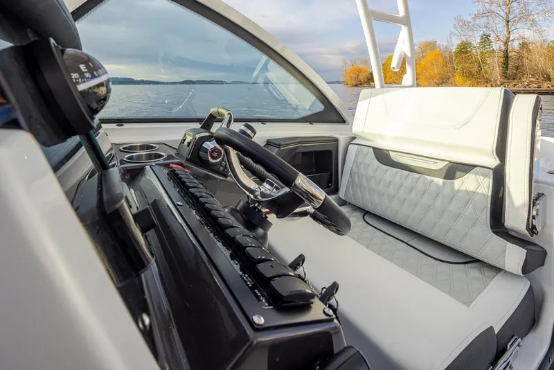 Slide: The Image of 2024 Blackfin 252 DC boat interior with steering wheel and seating, on a calm lake. - 13