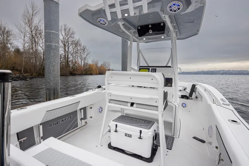Slide: The Image of 2024 Blackfin 222 CC boat interior with modern console and seating, docked on a calm lake. - 29