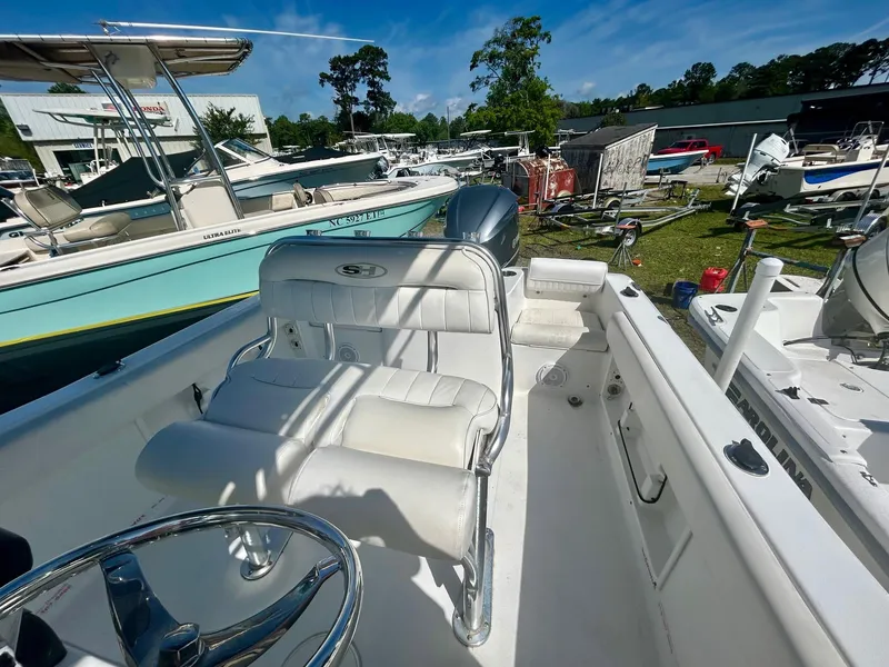 Slide: The Image of 2018 Sea Hunt Triton 225 boat interior with white seating and steering wheel, docked outdoors. - 6