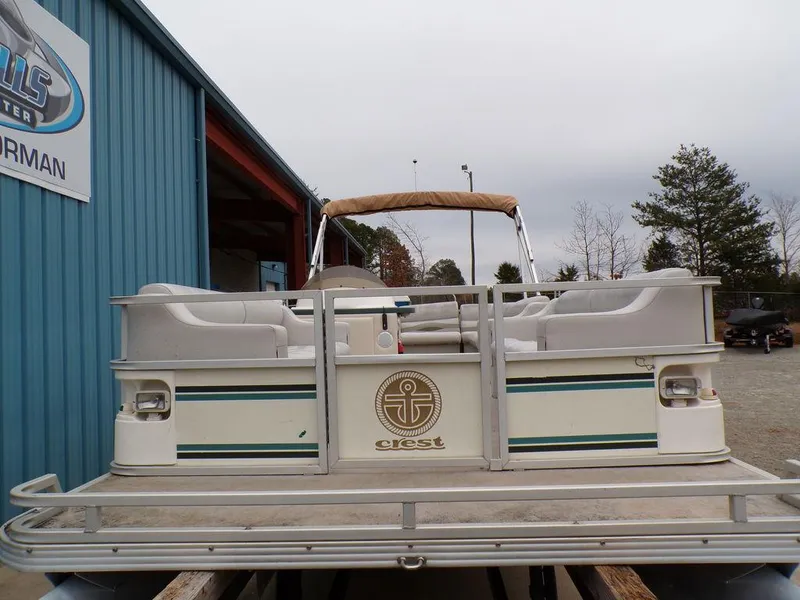 Slide: The Image of 2000 Crest Crest II DL pontoon boat with beige seating, docked near a blue building. - 3