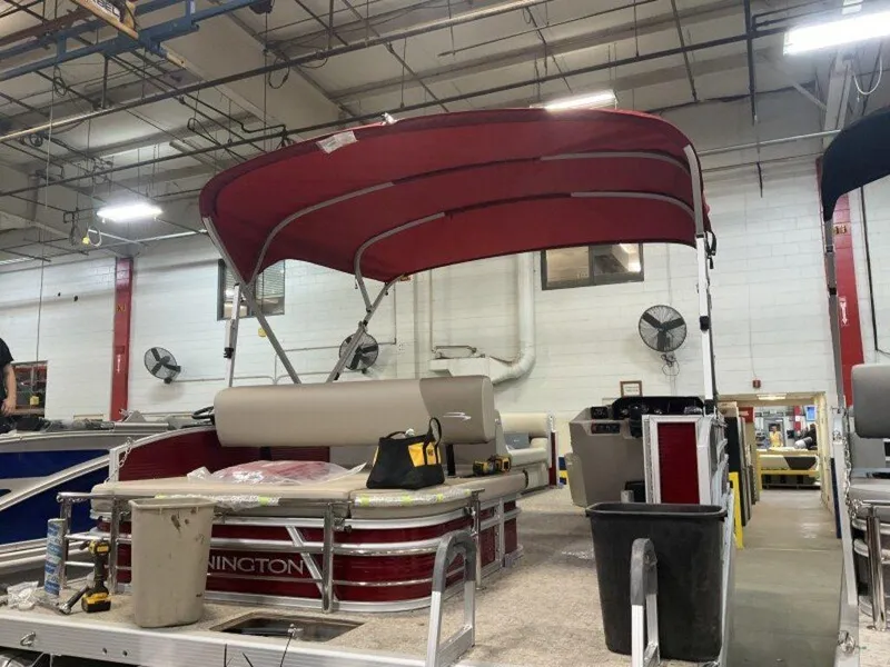 Slide: The Image of 2025 Bennington S Swingback 22 SSB pontoon boat in a factory setting with red canopy. - 16