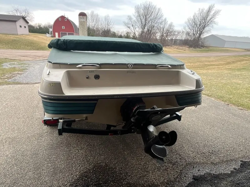 Slide: The Image of 1995 Celebrity 180 Bowrider boat, rear view, parked on driveway near rural landscape. - 3