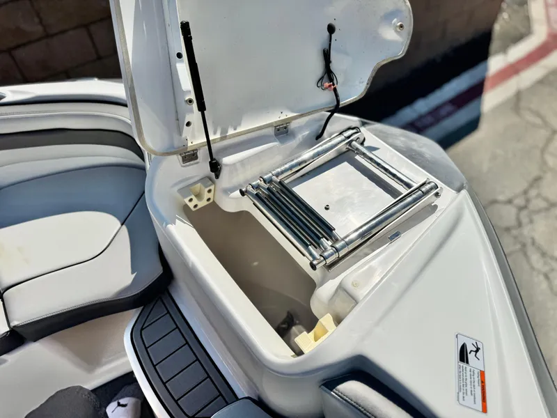 Slide: The Image of 2020 Yamaha AR240 boat storage compartment with ladder, open lid, and seating area. - 17