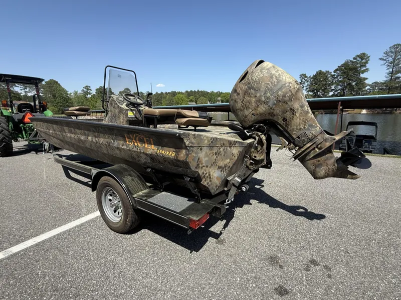 Slide: The Image of 2025 Excel Stalker Center Console 1960 boat on trailer, camouflage design, parked outdoors. - 2