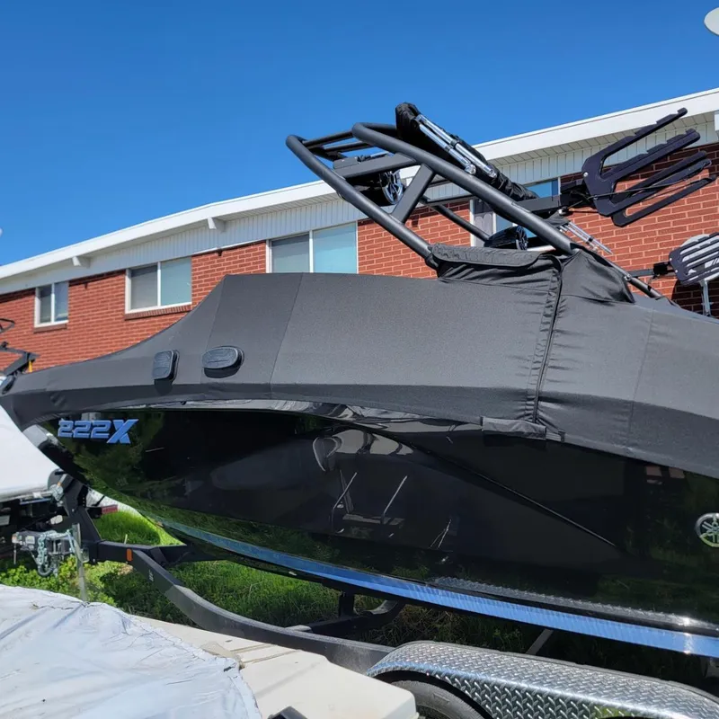 Slide: The Image of 2024 Yamaha Boats 222XD covered, parked near a brick building under a clear blue sky. - 2