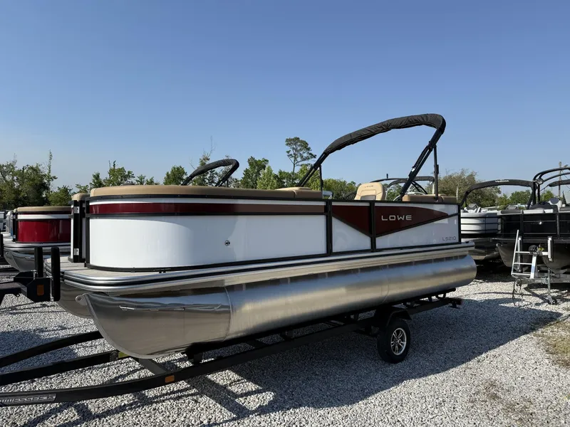 Slide: The Image of 2025 Lowe LS 210 pontoon boat on trailer, parked outdoors under clear blue sky. - 1