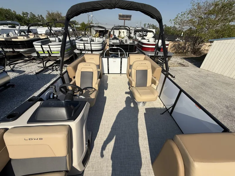 Slide: The Image of 2025 Lowe LS 210 pontoon boat interior with beige seating and steering console. - 2