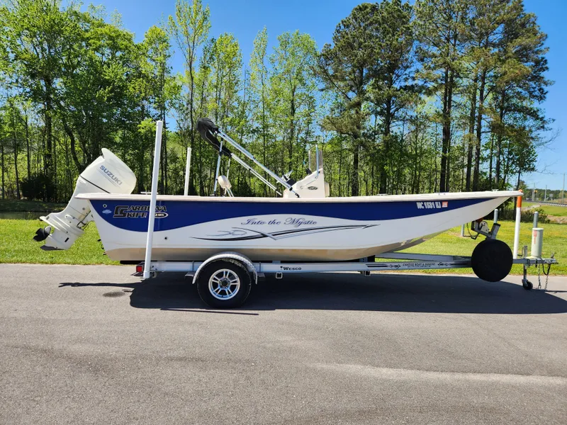 Slide: The Image of 2018 Carolina Skiff 218 DLV boat on trailer, parked outdoors with trees in background. - 0