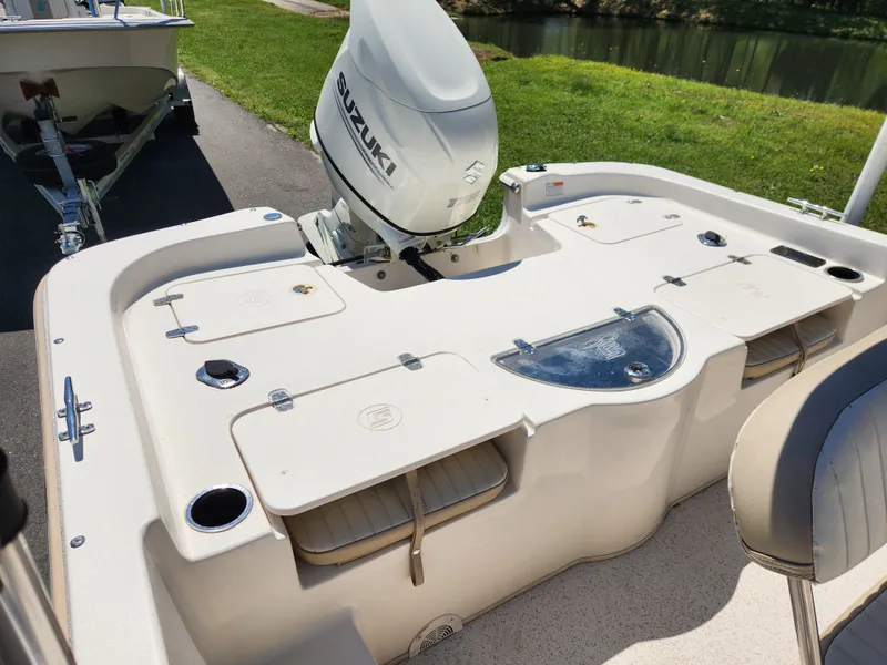 Slide: The Image of 2018 Carolina Skiff 218 DLV boat with Suzuki outboard motor, docked near a grassy area. - 10