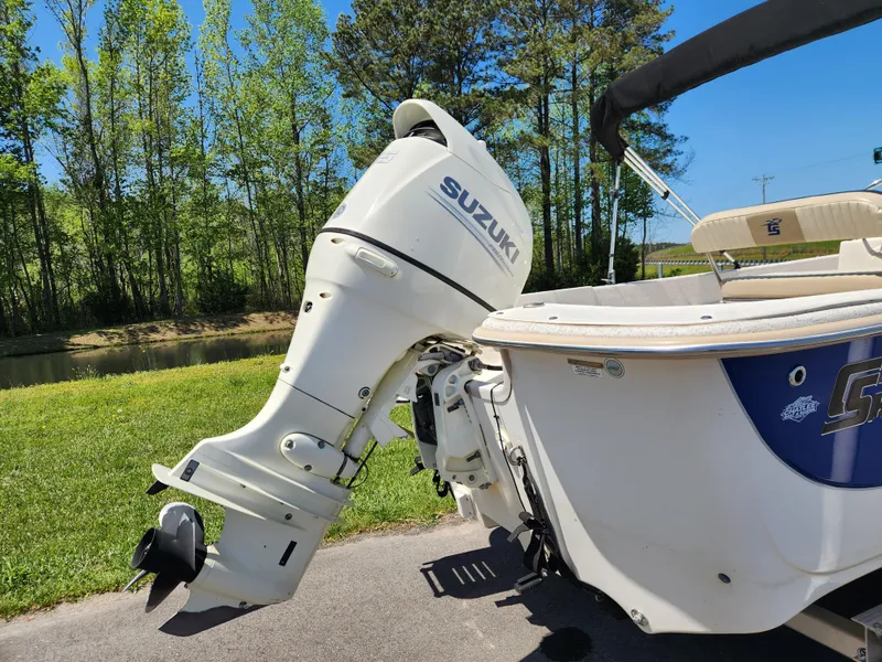 Slide: The Image of 2018 Carolina Skiff 218 DLV with Suzuki outboard motor, parked near a scenic waterway. - 3