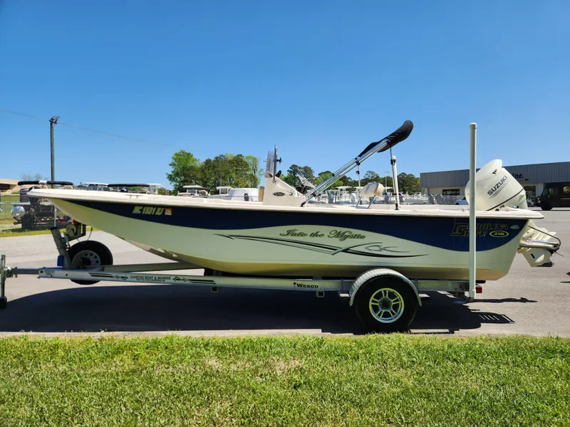 Slide: The Image of 2018 Carolina Skiff 218 DLV boat on trailer, parked outdoors under clear blue sky. - 6