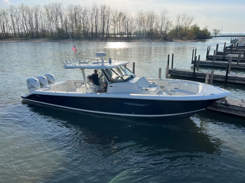 Slide: The Image of 2022 Pursuit S 378 Sport boat docked on a serene lake with trees in the background. - 11