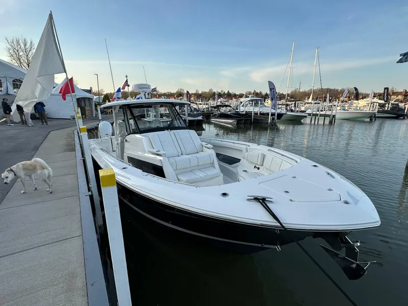 Slide: The Image of 2022 Pursuit S 378 Sport boat docked at marina, clear sky, flags, and a dog nearby. - 18