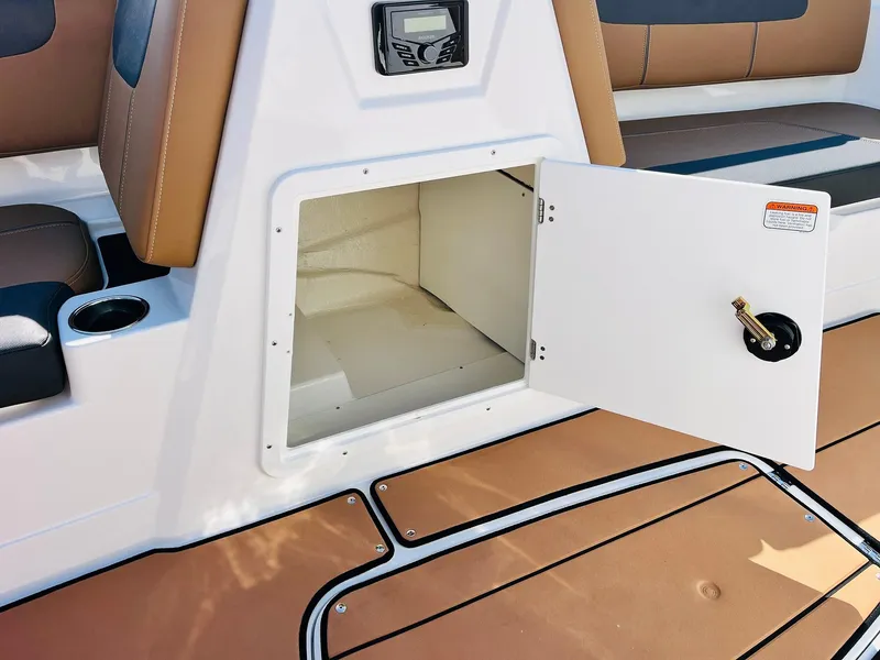 Slide: The Image of 2024 Tahoe 1950 boat storage compartment with open door, brown seating, and cup holder. - 24