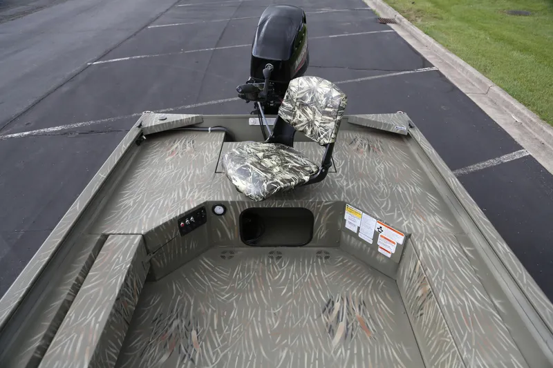 Slide: The Image of 2025 Tracker Grizzly 1654 T Sportsman boat with camo seat and motor, parked on pavement. - 3