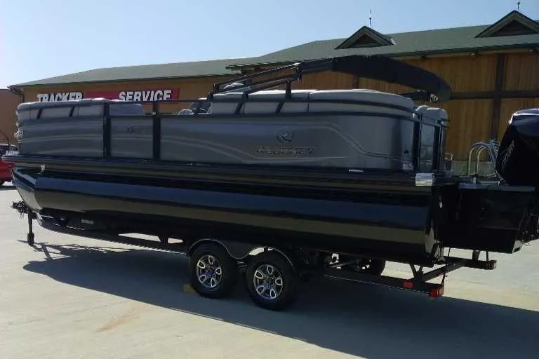Slide: The Image of 2024 Regency 230 DL3 pontoon boat on trailer, parked outside a service center. - 0