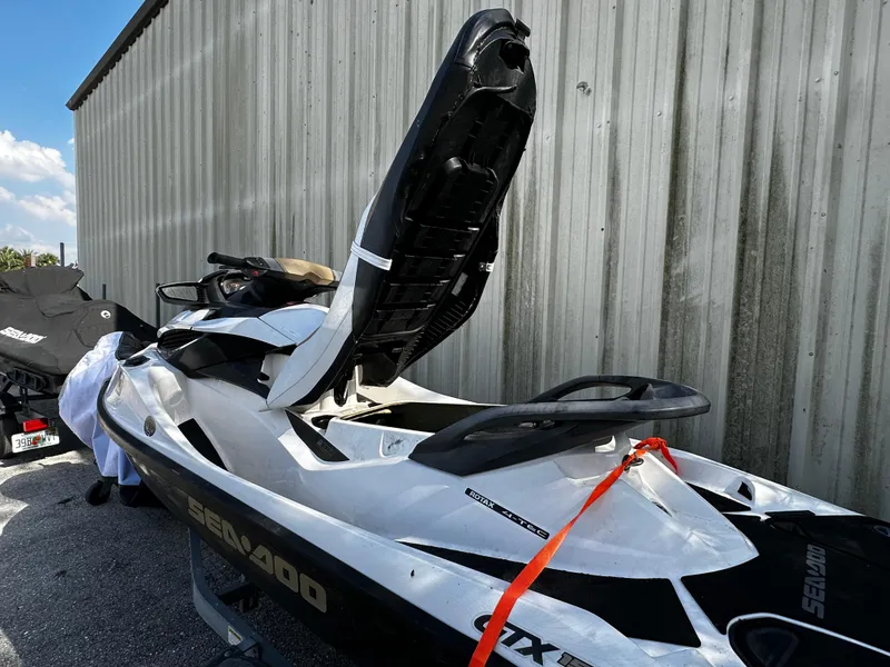 Slide: The Image of 2012 Sea-Doo GTX 155 jet ski with open seat storage, parked by a metal building. - 9
