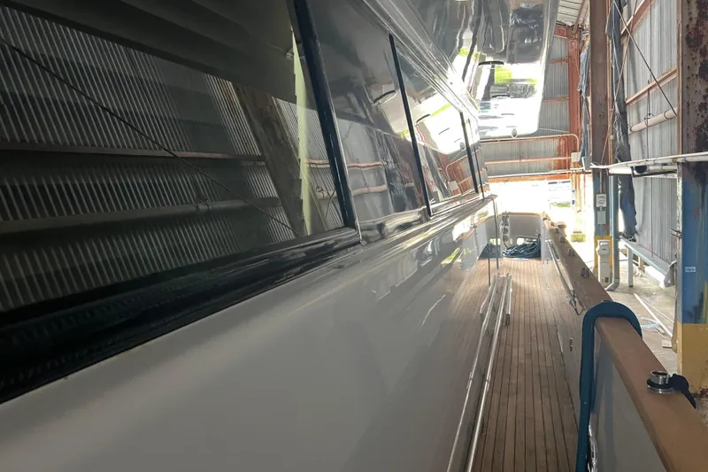 Slide: The Image of Side view of a 2001 Falcon 106 yacht in a shipyard, showcasing sleek design and wooden deck. - 19