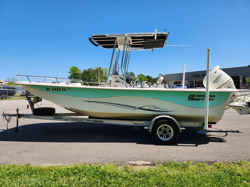 Slide: The Image of 2018 Carolina Skiff 218 DLV boat on trailer, parked outdoors under clear blue sky. - 6