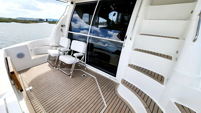 Slide: The Image of 2002 Cruisers 5000 yacht deck with chairs, wooden flooring, and stairs by the water. - 6