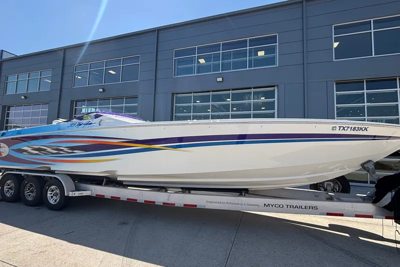 Slide: The Image of 2000 Cigarette 38' Top Gun boat on trailer, vibrant graphics, parked outside modern building. - 33