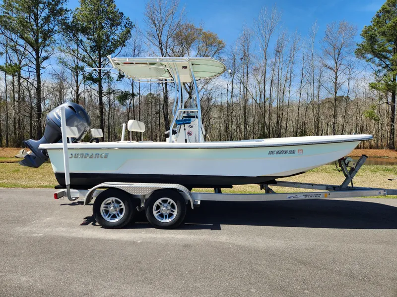 Slide: The Image of 2015 Sundance B20CCR boat on trailer, parked outdoors with trees in the background. - 0