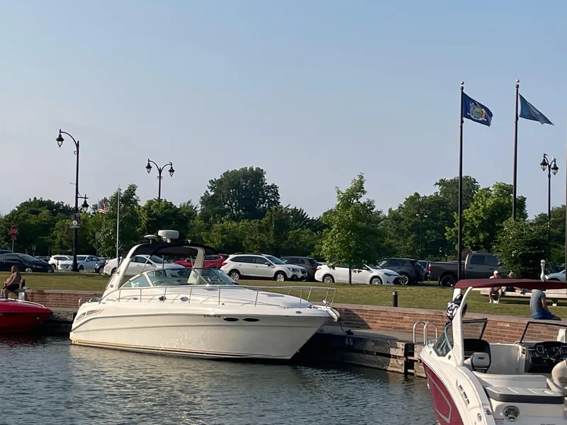 Slide: The Image of Sea Ray 340 Sundancer 2000 docked at marina with flags and parked cars in background. - 4