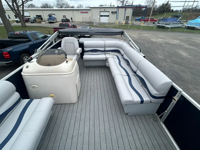 Slide: The Image of 1999 Sylvan 20 Cruise pontoon boat with spacious seating and helm, parked in a lot. - 6