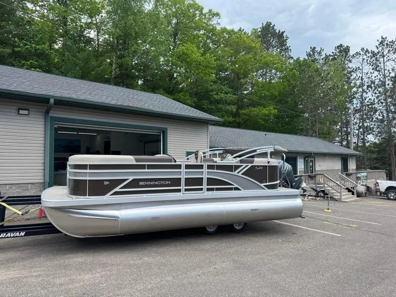 Slide: The Image of 2025 Bennington 20SSR pontoon boat parked outside a building, surrounded by trees. - 2