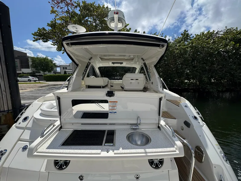 Slide: The Image of 2019 Sea Ray Sundancer 350 Coupe with open cockpit kitchen and sink, docked by lush greenery. - 2