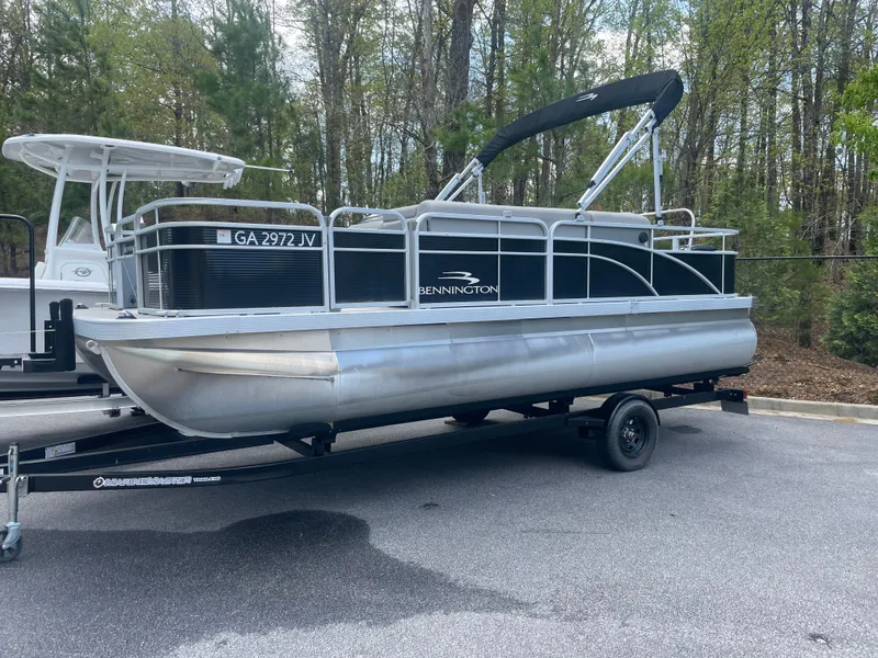 Slide: The Image of 2023 Bennington 20SV pontoon boat on trailer, parked in wooded area. - 1