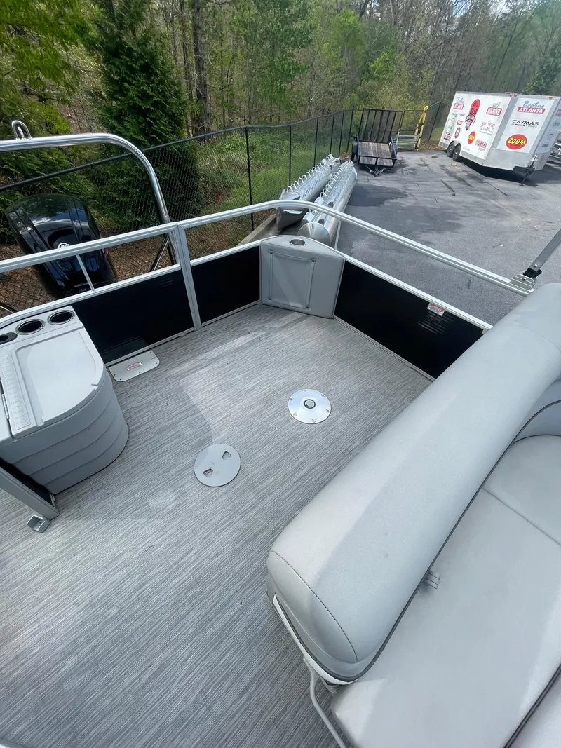 Slide: The Image of 2023 Bennington 20SV pontoon boat deck with seating and cup holders, parked outdoors. - 7