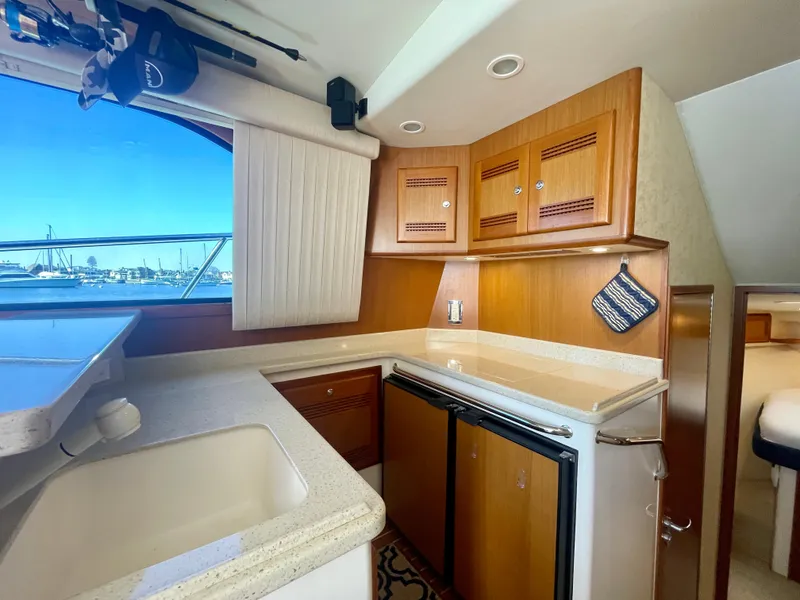 Slide: The Image of 2006 Cabo 40 Flybridge yacht interior with kitchenette, featuring wood cabinets and a compact fridge. - 43