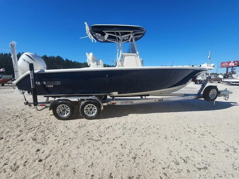 Slide: The Image of 2025 Pathfinder 2400 Open boat on trailer, parked on sandy ground under clear blue sky. - 2