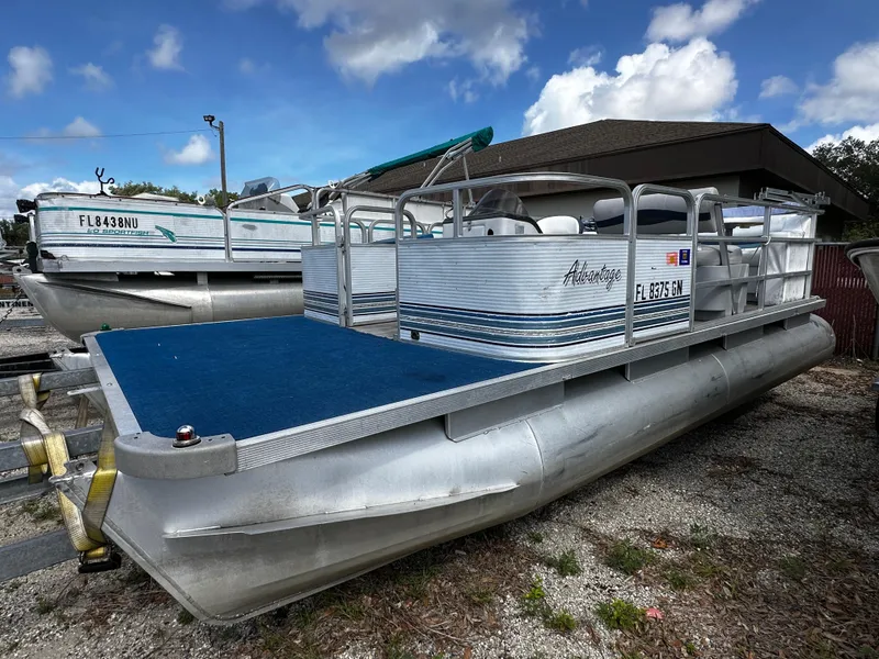 Slide: The Image of 1994 Sylvan Adventure pontoon boat with blue deck, parked outdoors under a cloudy sky. - 1