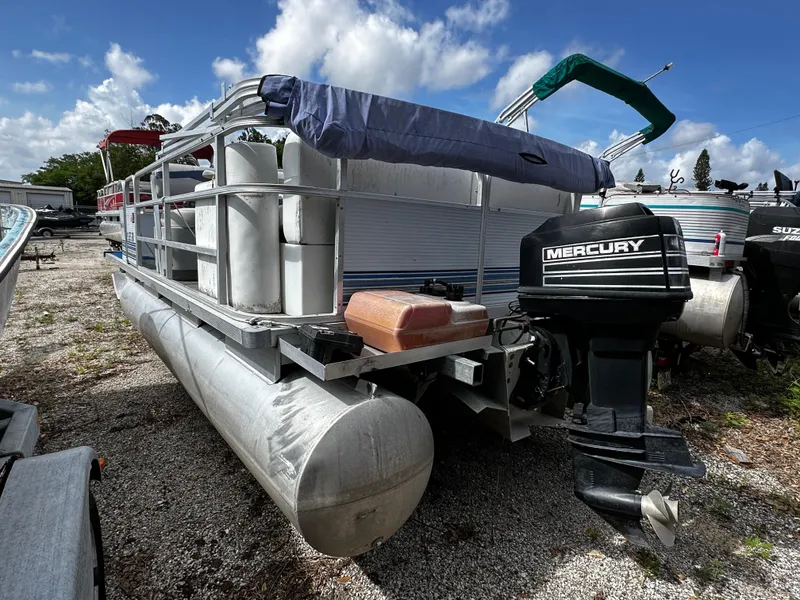 Slide: The Image of 1994 Sylvan Adventure pontoon boat with Mercury outboard motor, parked on gravel under blue sky. - 2