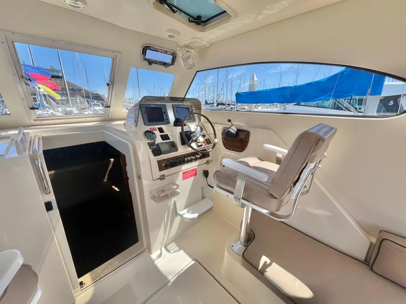 Slide: The Image of 2006 Mainship Pilot 30-II Sedan interior with helm, seating, and marina view. - 10