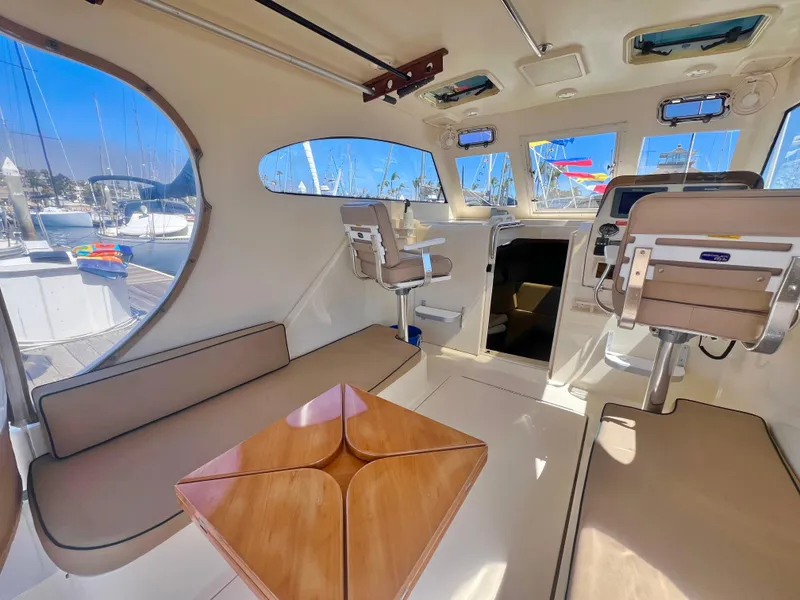 Slide: The Image of 2006 Mainship Pilot 30-II Sedan interior with seating, table, and helm, docked at marina. - 7