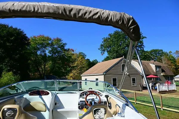 Slide: The Image of 2015 Crownline 236 SC boat with canopy, parked near a house under clear blue sky. - 38