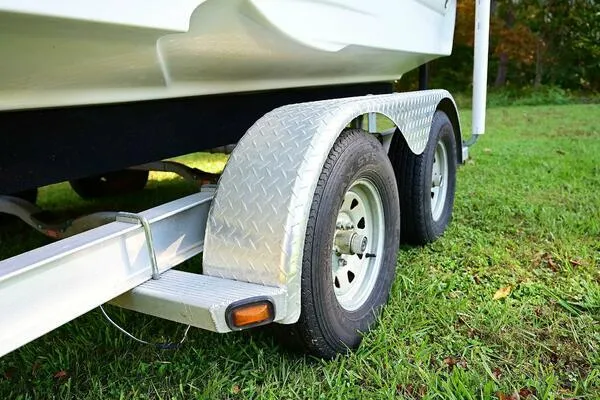 Slide: The Image of Trailer for 2015 Crownline 236 SC boat on grass, featuring dual wheels and metal fenders. - 47