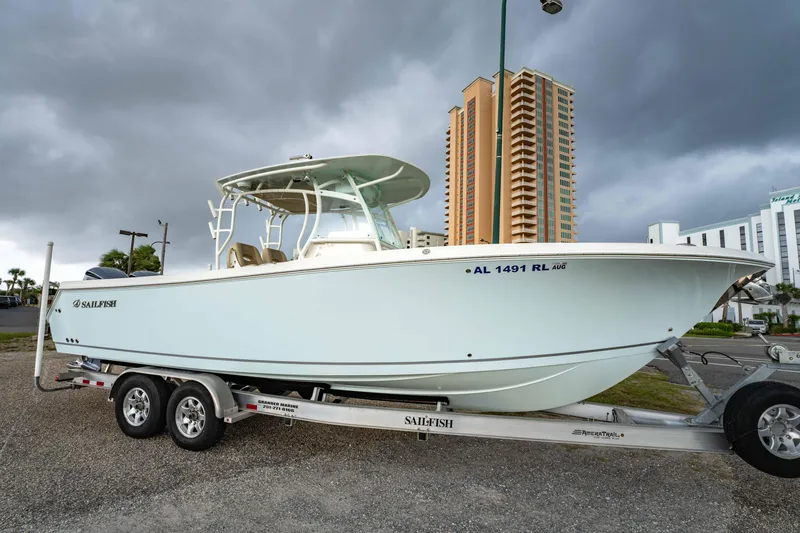Slide: The Image of 2018 Sailfish 290 CC boat on trailer, parked near tall buildings under cloudy sky. - 34